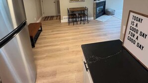 A modern kitchen with a stainless steel refrigerator, a dining area with a wooden table and chairs, and a kitchen island. There is a decorative wall piece and a motivational sign on the wall.