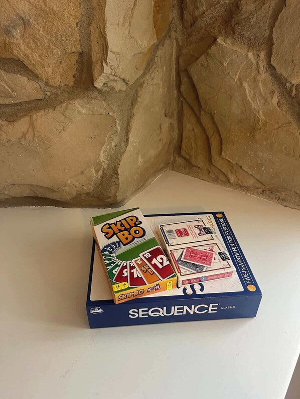 A game box labeled 'SEQUENCE' with 'SKIPBO' and 'GOLIATH' on it, placed on a white surface against a stone wall. - Newly remodeled MIL Suite-Long&short term ok (Savage)