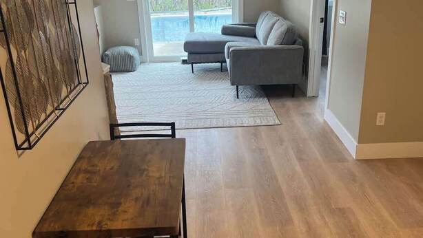 A spacious living area with a wooden dining table, a gray sofa, and a large window offering a view of trees.