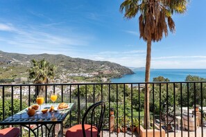 A balcony with a table set for breakfast, overlooking a coastal landscape with hills and a clear sky. - Faro's Sun Beach Villa in Almuñecar (Almuñécar)