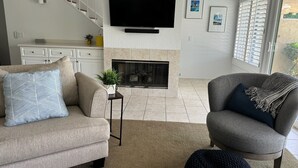 A living room with a fireplace, a sofa, a chair, and a TV mounted on the wall. - Beautiful and charming condo in Woodhaven Country Club! Recently updated (Palm Desert)