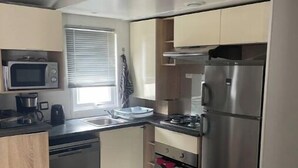 A compact kitchen with a microwave, stove, and refrigerator. There is a dining table with chairs and a window with blinds.