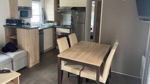 A compact kitchen with a microwave, stove, and refrigerator. There is a dining table with chairs and a sofa in the living area.
