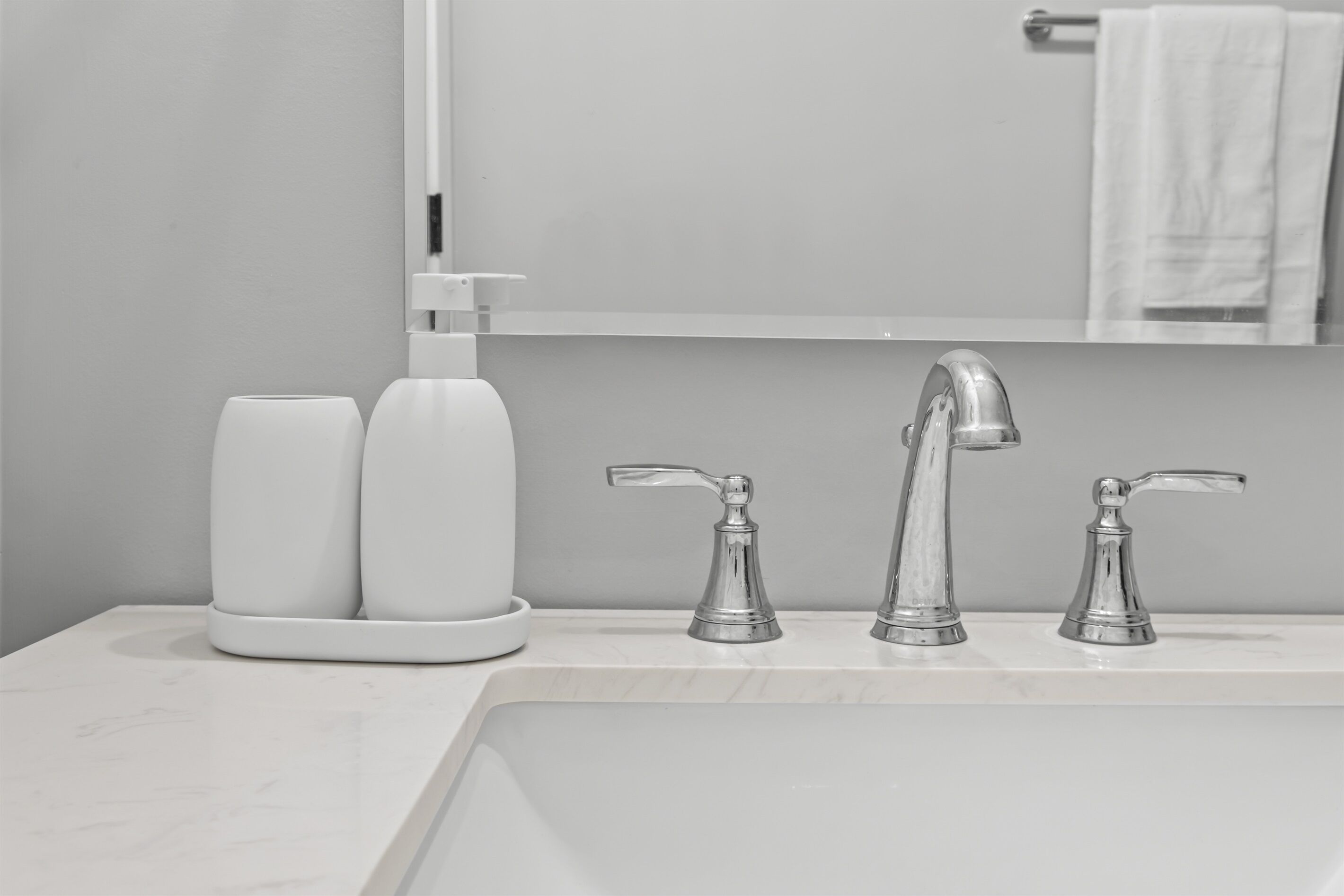 A bathroom with a white sink, two faucets, and two white bottles on the counter.