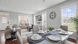 Een moderne eetruimte met een tafel voor vier personen, een bank en een aan de muur bevestigde televisie.
