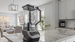 Een moderne keuken met een ingebouwde blender op het aanrecht, een eethoek met een tafel en stoelen, en een groot raam dat voor natuurlijk licht zorgt.