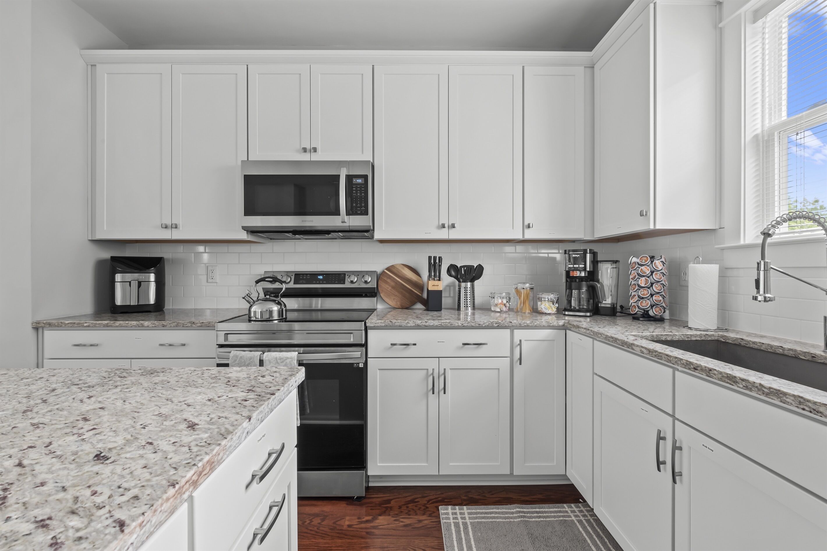 A modern kitchen with white cabinets, stainless steel appliances, and a granite countertop.