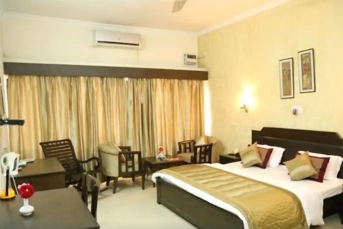 Habitación de hotel con cama, escritorio, silla y mesa. Cortinas en la ventana, y un equipo de aire acondicionado instalado en la pared.