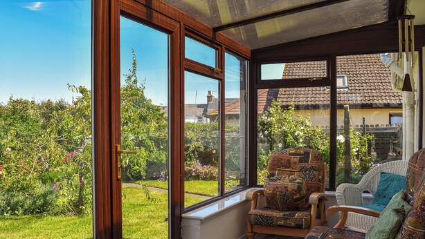 Habitació il·luminada pel sol, amb grans finestres, mobles de vimet i vista a un jardí.