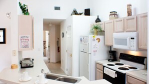 A compact kitchen with a white countertop, a refrigerator, a microwave, a stove, and wooden cabinets. - Andy's Westridge Villa (Davenport)