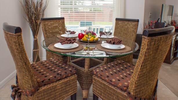 A dining table with four wicker chairs, a glass top, and a fruit centerpiece. - Andy's Westridge Villa (Davenport)