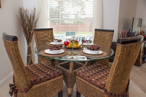 A dining table with four wicker chairs, a glass top, and a fruit centerpiece.