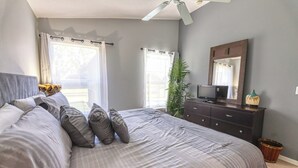 Een slaapkamer met een groot bed, een dressoir, een televisie en een plafondventilator.