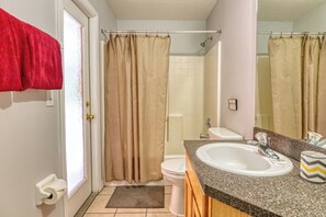 A bathroom with a shower curtain, toilet, sink, and a towel rack with a red towel. - Camile's Sandy Ridge Vacation Home (Davenport)