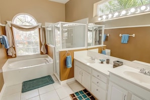 A bathroom with a bathtub, two sinks, a vanity, and a large mirror with lights. - Ron's Highlands Reserve Vacation Home (Davenport)