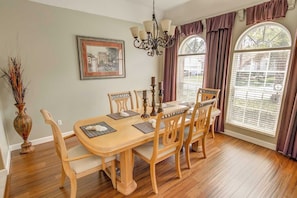 A dining room with a wooden table, six chairs, a chandelier, a framed picture, and large windows with curtains. - Ron's Highlands Reserve Vacation Home (Davenport)