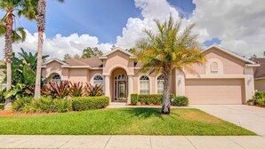 A two-story house with a front entrance, a garage, and a well-maintained lawn with tropical plants.