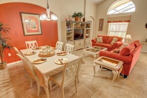 A living room with a dining table set for four, a red sofa, and a television in the background.