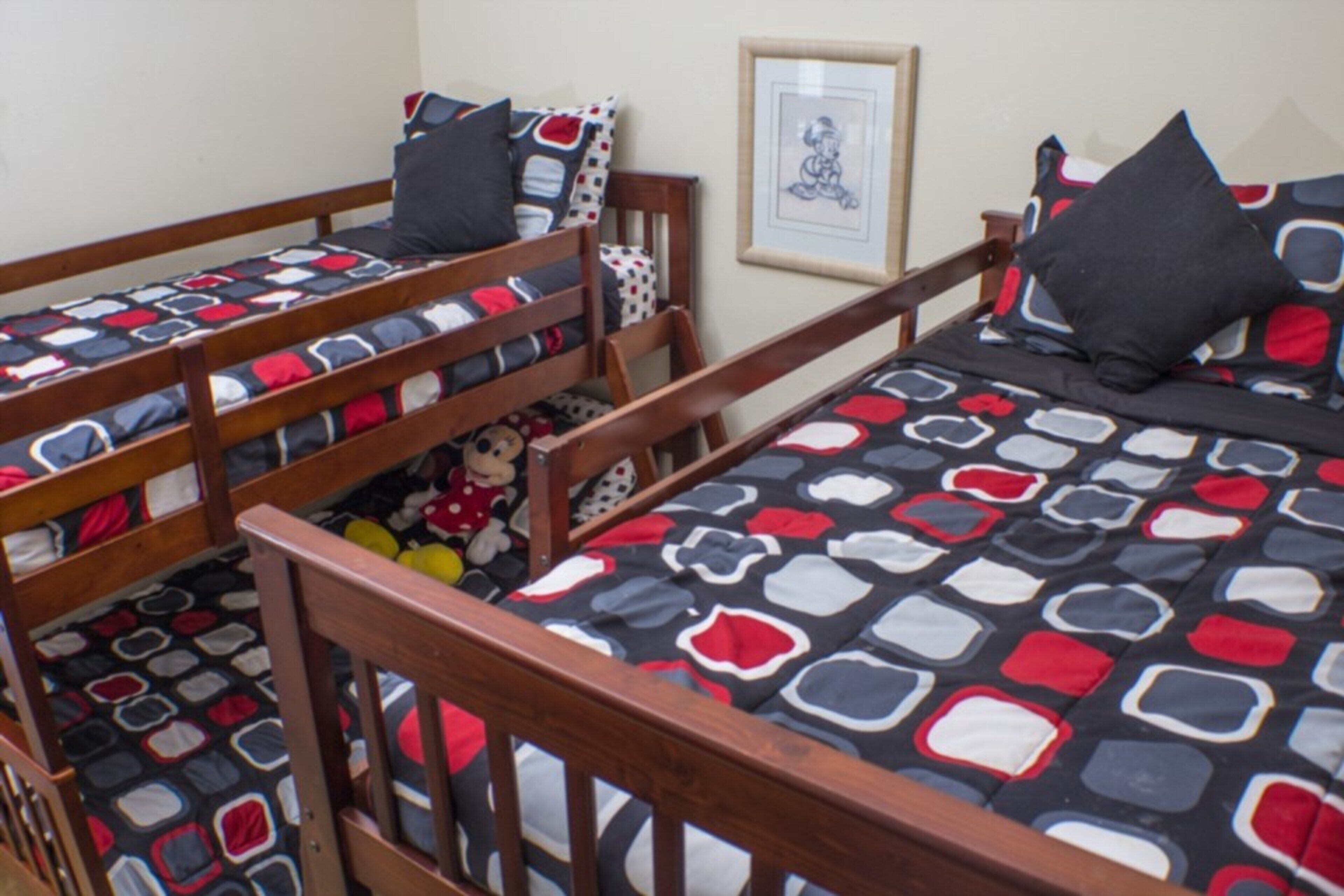 Une chambre avec trois lits superposés en bois, chacun recouvert d’une courtepointe à motifs.