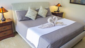 Ein ordentlich gemachtes Bett mit weißer Decke und zwei Kissen, ein Nachttisch mit Lampe und ein Wandbild.