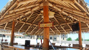A tiki bar with a thatched roof, wooden beams, and a sign reading "TIKI BAR".