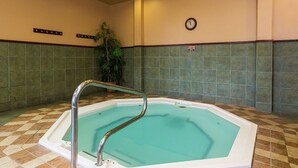 A rectangular indoor pool with a metal safety railing, surrounded by green-tiled walls and a checkered floor pattern.