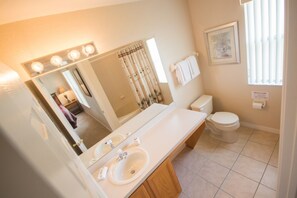 Une salle de bain avec un grand miroir, deux lavabos, des toilettes et un rideau de douche.
