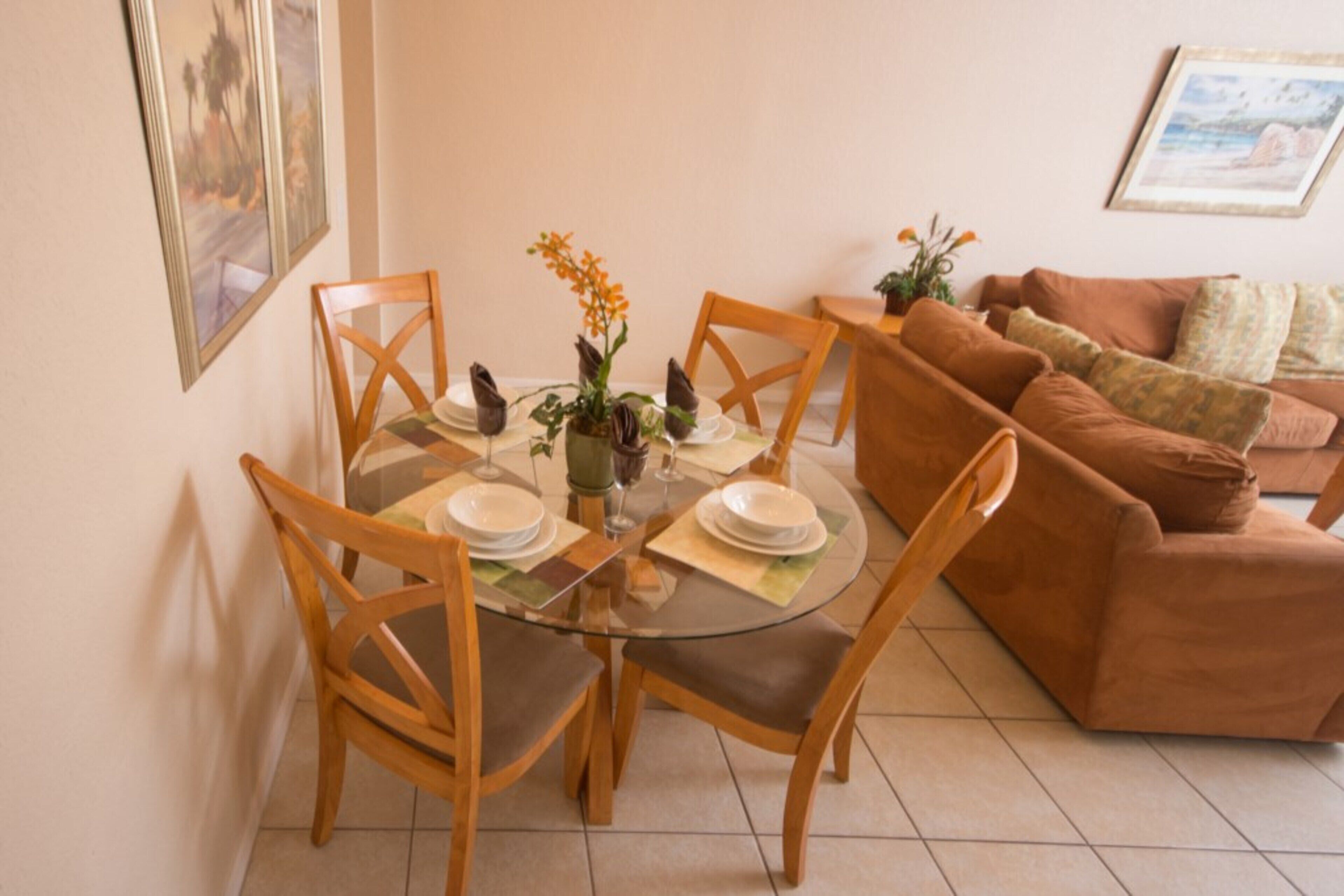 Un comedor con mesa de vidrio, sillas de madera y sofá marrón.