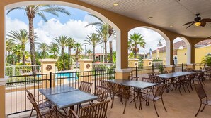 An outdoor patio with tables and chairs, a pool, and palm trees.