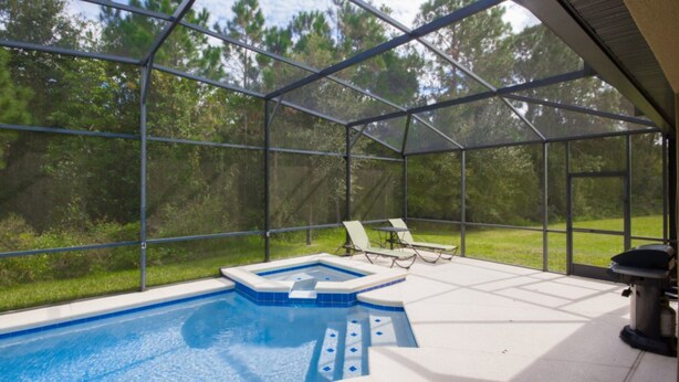 A covered outdoor swimming pool with clear glass walls, surrounded by a patio area with lounge chairs. - Robert's Cypress Pointe Vacation Home (Davenport)