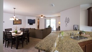 A modern kitchen with granite countertops, a dining area with a table and chairs, and a living room with a sofa. - Robert's Cypress Pointe Vacation Home (Davenport)