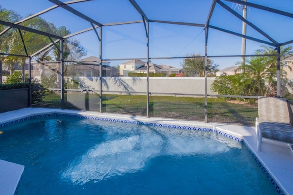 Una piscina con cerramiento de vidrio, rodeada por un muro de concreto y un jardín cubierto de césped.