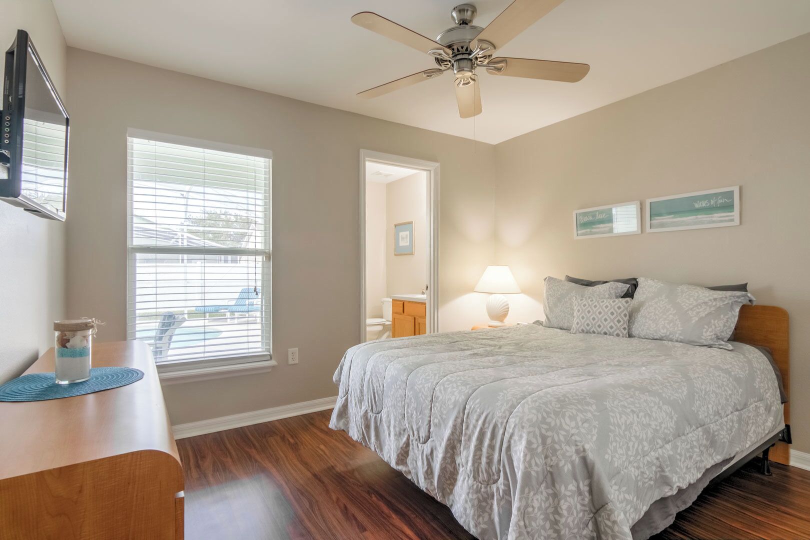 A bedroom with a bed, a ceiling fan, a window with blinds, a bedside table, and a nightstand.