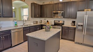 A modern kitchen with dark cabinets, stainless steel appliances, a granite countertop, and a small island with a flower arrangement. - The Stirling Luxury Solterra Vacation Home (Davenport)