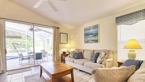 Un salon comprenant un canapé, une table basse et des lampes. Une porte vitrée donne accès à un espace extérieur aménagé avec des chaises et une table.
