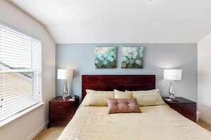 A bedroom with a large bed, two nightstands, a wooden headboard, and two wall-mounted paintings. - TIm and Helen's West Haven Vacation Home (Davenport)