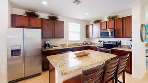 Eine moderne Küche mit Granit-Arbeitsplatten, Edelstahlgeräten, Holzschränken und einer zentralen Kochinsel mit Barhocker.