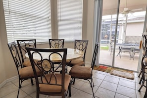 A dining area with a round table and six chairs, large windows with blinds, and a view of an outdoor patio with additional seating. - The Hill at Highlands Reserve (Davenport)