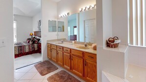 A modern bathroom with wooden cabinets, a large mirror with lights, a bathtub, and a window with blinds. - Len & Arlene's Tuscan Ridge Vacation Home (Davenport)