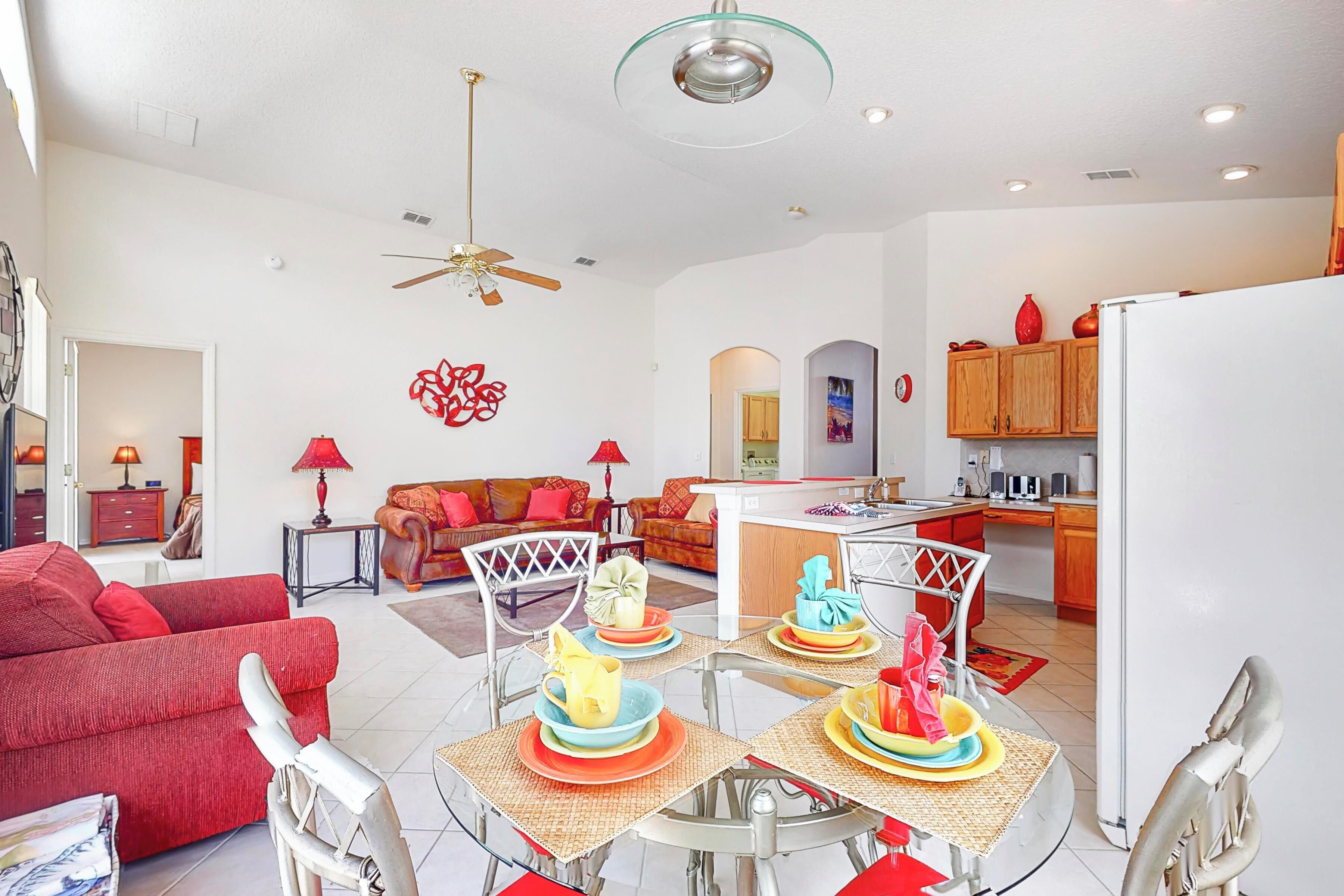 A modern living room with a red sofa, a dining table with colorful plates, and a kitchen area with wooden cabinets.