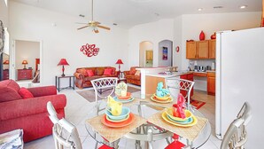 A modern living room with a red sofa, a dining table with colorful plates, and a kitchen area with wooden cabinets. - Len & Arlene's Tuscan Ridge Vacation Home (Davenport)