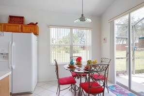 Eine Küche mit Kühlschrank, Esstisch mit Stühlen, einer Pendelleuchte und einem Fenster mit Jalousien.