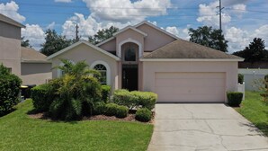 A single-story house with a garage, a front entrance, and a small front yard with shrubs and a palm tree. - Len & Arlene's Tuscan Ridge Vacation Home (Davenport)
