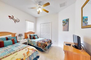 Ein Schlafzimmer mit zwei Betten, einem Deckenventilator, einem Schreibtisch mit Computer und Bildern an den Wänden.