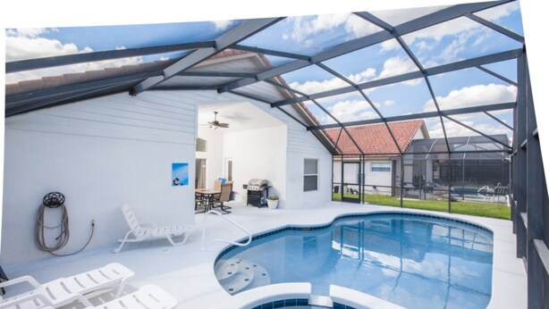 A swimming pool with a glass enclosure, lounge chairs, and a patio area. - Rafael's Solana Resort Vacation Home (Davenport)