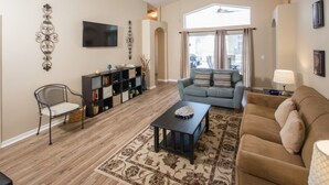 A living room with a sofa, armchair, coffee table, and bookshelf. - Rafael's Solana Resort Vacation Home (Davenport)