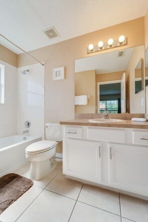 A modern bathroom with a bathtub, toilet, and vanity with a large mirror and lights.