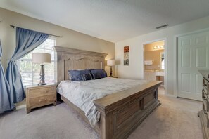 A bedroom with a large bed, wooden headboard, two bedside tables with lamps, a dresser, and a door leading to a bathroom.