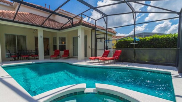 A swimming pool with red lounge chairs, a covered patio, and a tiled roof. - Jagjit's Tuscan Hills Vacation Home (Davenport)