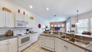 A kitchen with white cabinets, a stove, a microwave, and a dishwasher. There is a large island with a sink and a ceiling fan. - Jagjit's Tuscan Hills Vacation Home (Davenport)